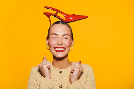 Улыбающаяся девушка с красной туфлей на голове на жёлтом фоне