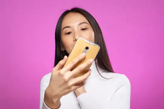 Азиатская девушка смотрит в смартфон на розовом фоне
