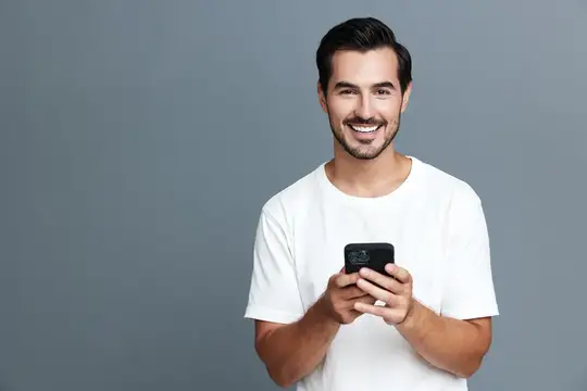 Улыбающийся мужчина в белой футболке держит смартфон на сером фоне