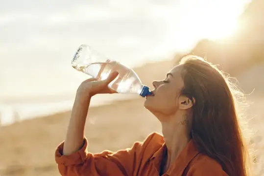 Молодая женщина пьёт воду из бутылки на закате