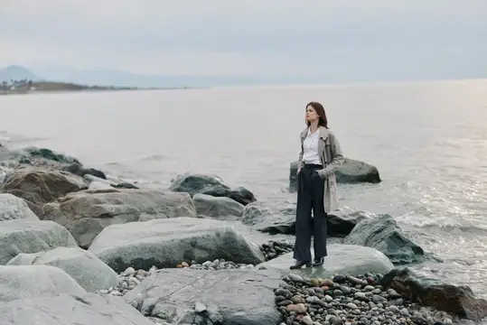 Молодая женщина стоит на камнях у моря в пасмурный день