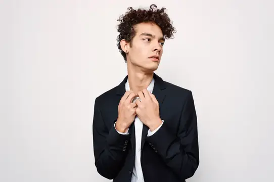 Кудрявый парень в тёмном пиджаке поправляет воротник рубашки