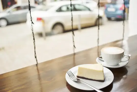 Кусок чизкейка и чашка кофе на столе у окна