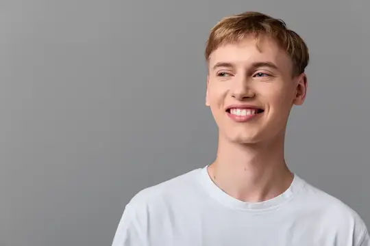 Улыбающийся светловолосый парень в белой футболке на сером фоне