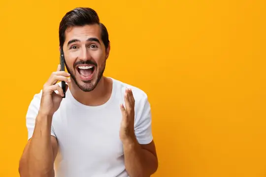 Удивлённый бородатый мужчина с телефоном на жёлтом фоне