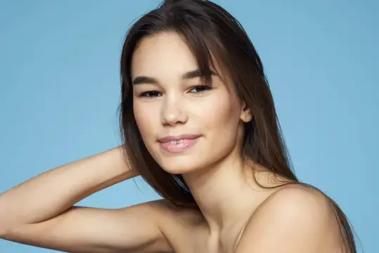 Молодая темноволосая женщина с лёгкой улыбкой на голубом фоне