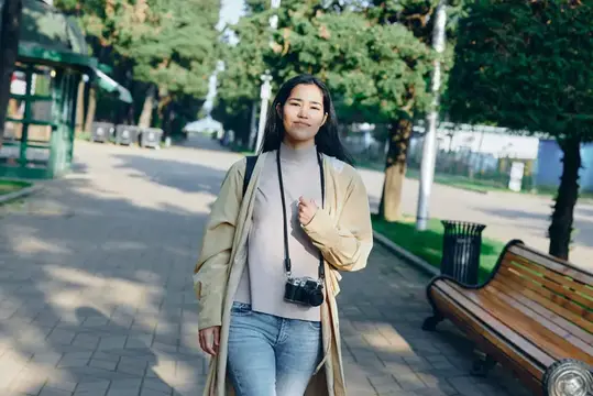 Молодая азиатская девушка с фотокамерой гуляет по аллее парка