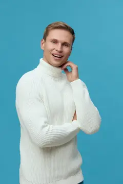 Улыбающийся блондин в белом свитере на голубом фоне