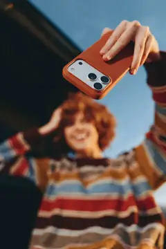 Рыжеволосая девушка держит смартфон в терракотовом чехле на фоне неба