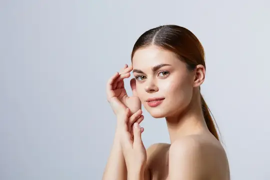Молодая женщина с гладкой кожей касается лица на сером фоне