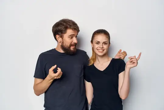 Бородатый мужчина и улыбчивая девушка показывают пальцами сердечко