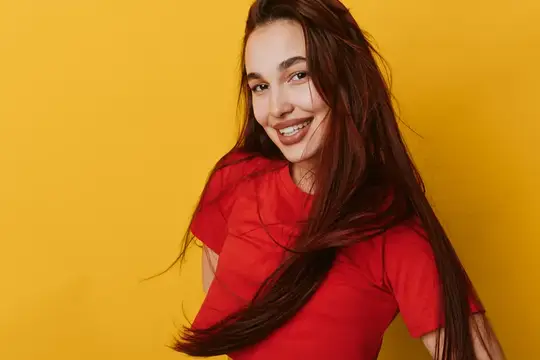 Улыбающаяся темноволосая девушка в красной футболке на жёлтом фоне