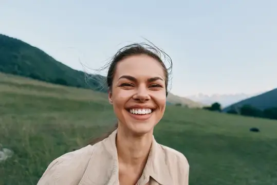 Улыбающаяся темноволосая женщина на фоне горного луга