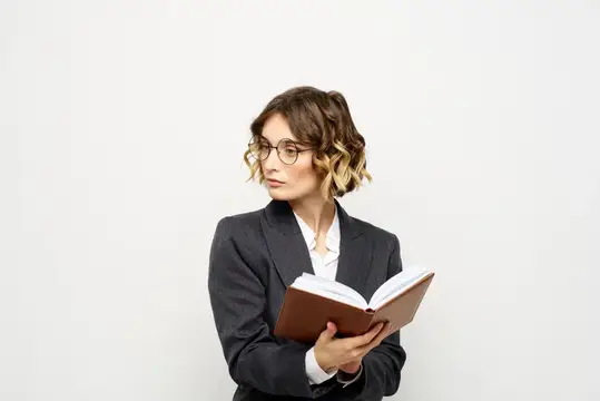Молодая женщина в очках и строгом пиджаке читает книгу на белом фоне