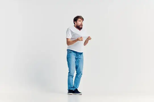 Бородатый мужчина в белой футболке удивлённо смотрит на разорванную бумагу