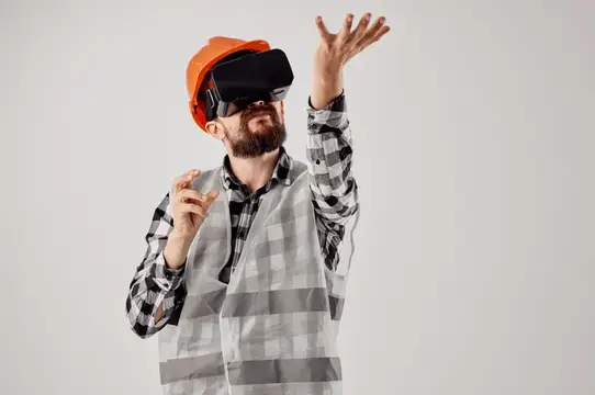 Бородатый мужчина в каске и VR-очках тянется рукой вверх