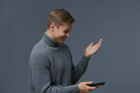 Улыбающийся мужчина в сером свитере жестом показывает на смартфон