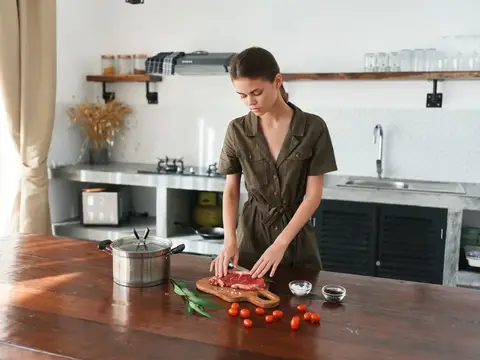 Молодая женщина в платье нарезает мясо на кухне