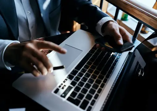 Мужчина в костюме работает за ноутбуком с телефоном в руке