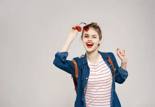 Весёлая молодая женщина в модной одежде, с рюкзаком, студентка, обучающая подростка, на сером фоне