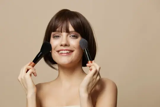 Женщина с кистями для макияжа возле лица, обнажённые плечи
