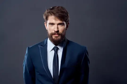 Бородатый мужчина в синем костюме на тёмном фоне