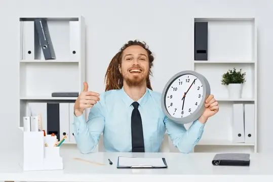 Веселый бизнесмен работает за столом, на котором стоят часы, в офисе