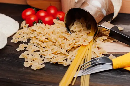 Макароны бантики рассыпаны из ковша рядом с помидорами