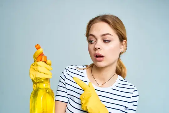 Удивлённая девушка в жёлтых перчатках с бутылкой чистящего средства