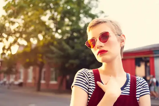 Стриженная девушка в красных очках на закате у кирпичного дома