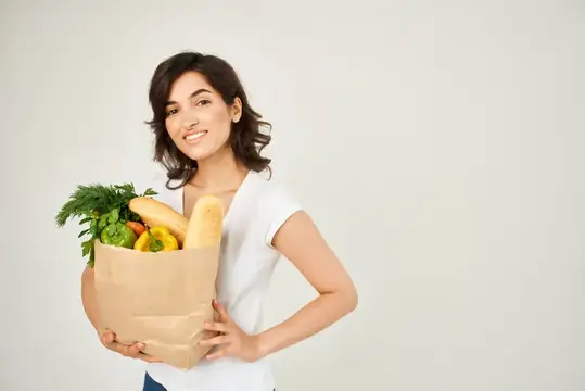Весёлая женщина с пакетом продуктов из супермаркета на светлом фоне