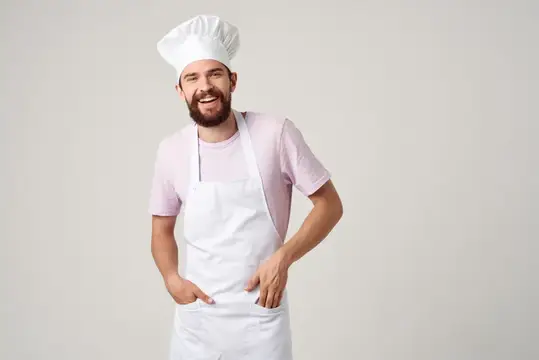 Улыбающийся бородатый повар в колпаке и фартуке на светлом фоне