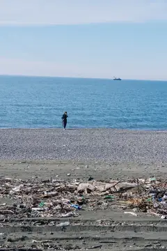Одинокий человек стоит на галечном пляже среди мусора