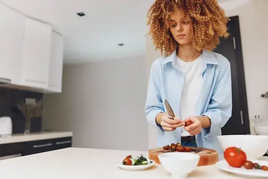 Кудрявая девушка режет помидоры на кухне