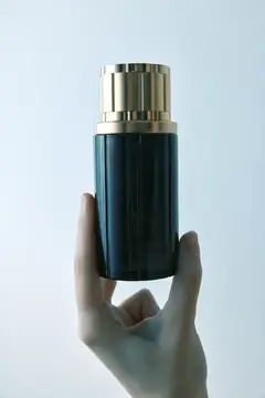 Рука держит тёмно-зелёный флакон с золотой крышкой на светлом фоне