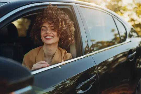 Улыбающаяся кудрявая девушка выглядывает из окна автомобиля