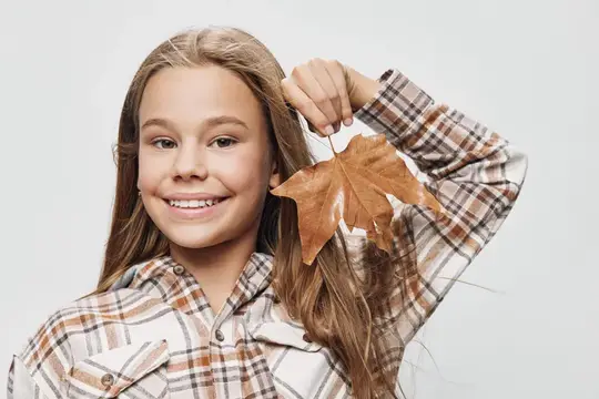 Улыбчивая девочка с кленовым листом в клетчатой рубашке