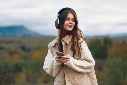 Улыбающаяся девушка в наушниках со смартфоном на осенней прогулке