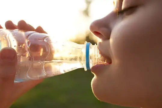 Женщина пьёт воду из пластиковой бутылки на открытом воздухе летом, крупный план