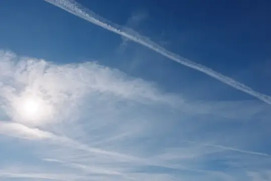 След самолёта в синем небе с перистыми облаками и солнцем