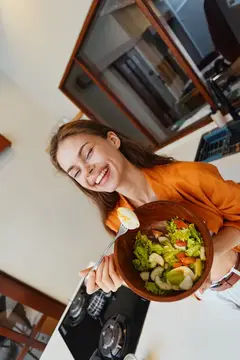 Улыбающаяся девушка с миской овощного салата на кухне