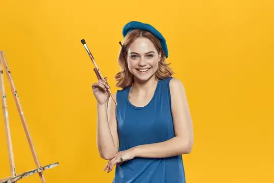 Улыбающаяся девушка-художница с кистью в синем берете на желтом фоне