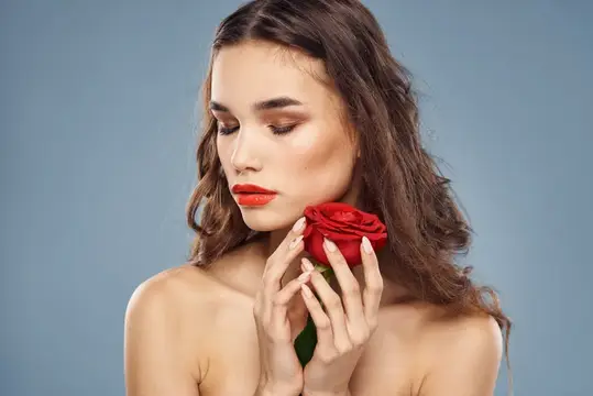 Молодая женщина с красной розой у лица на сером фоне