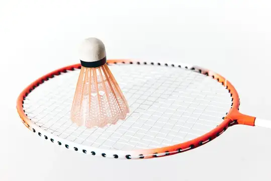 Волан лежит на струнах бадминтонной ракетки на белом фоне