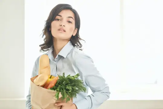 Молодая женщина с бумажным пакетом продуктов у окна