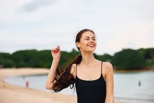 Улыбающаяся темноволосая девушка в купальнике на песчаном пляже