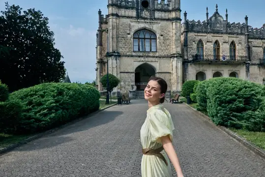 Улыбающаяся девушка в светлом платье на фоне старинного замка