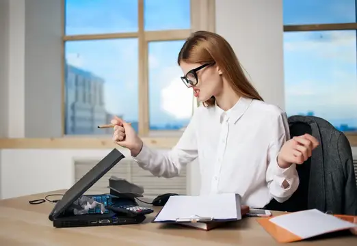 Девушка в очках с блокнотом работает за ноутбуком в офисе