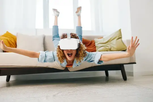 Кудрявая женщина в VR-очках лежит на диване с раскинутыми руками