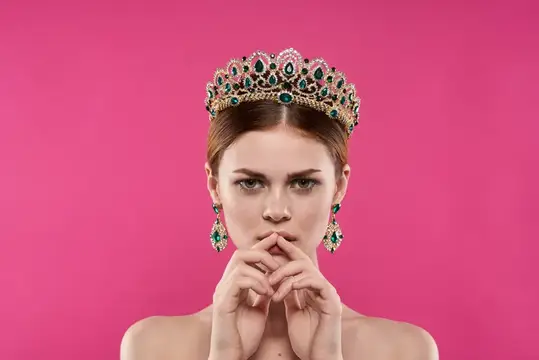 Привлекательная женщина в короне на голове, макияж, украшения, розовый фон